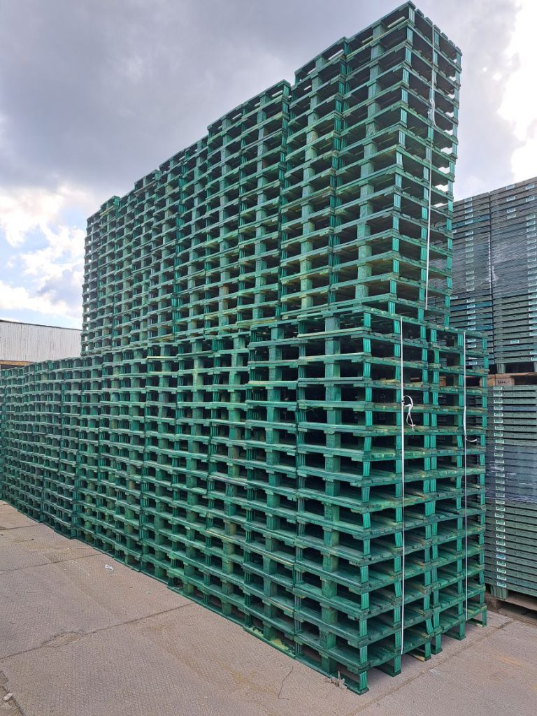 Large stacks of green pallets stored in an outdoor logistics yard.